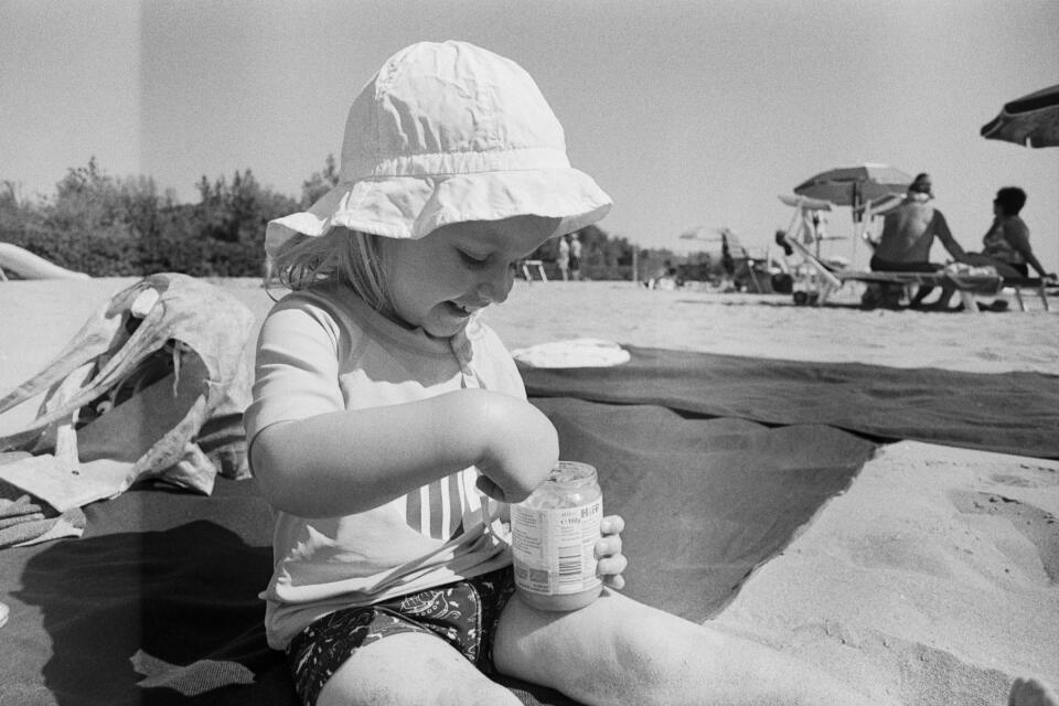 Zoe sitting at the beach, smiling and looking down into her glass of fruit with a spoon in her hand.