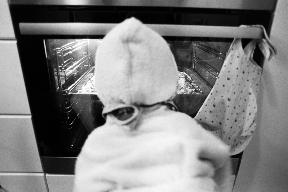 Zoe in bathrobe in front of our oven, looking at the pizza that's baking inside.