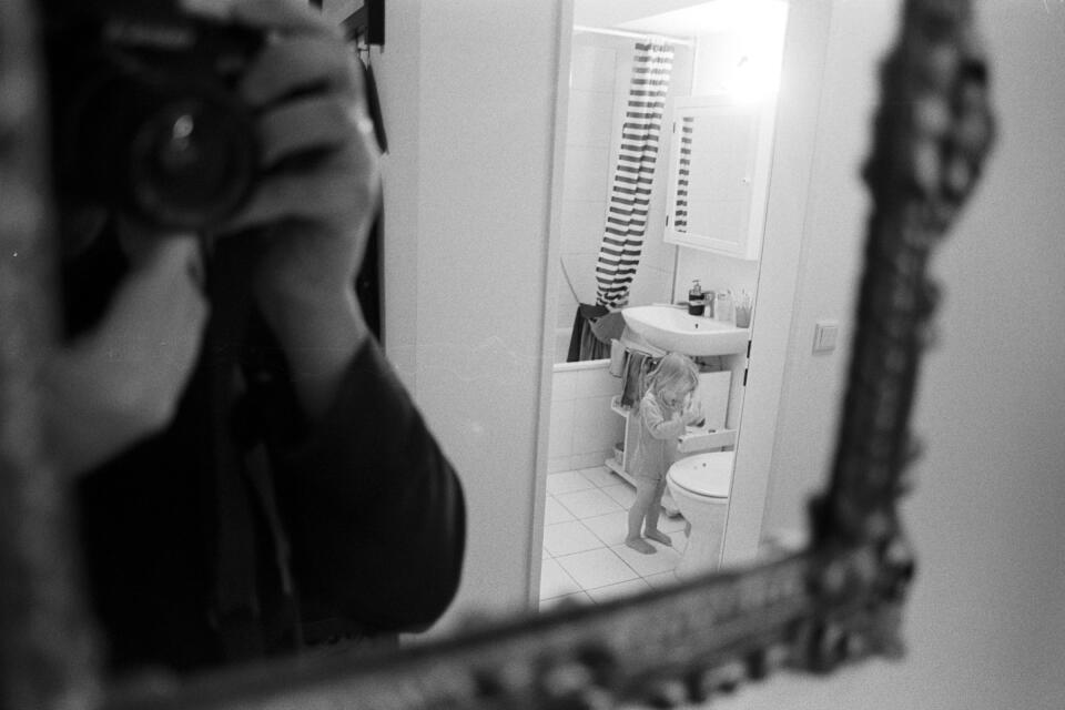 Zoe in the bathroom, photographed via a reflection in the mirror, that also contains the camera itself and my two hands.