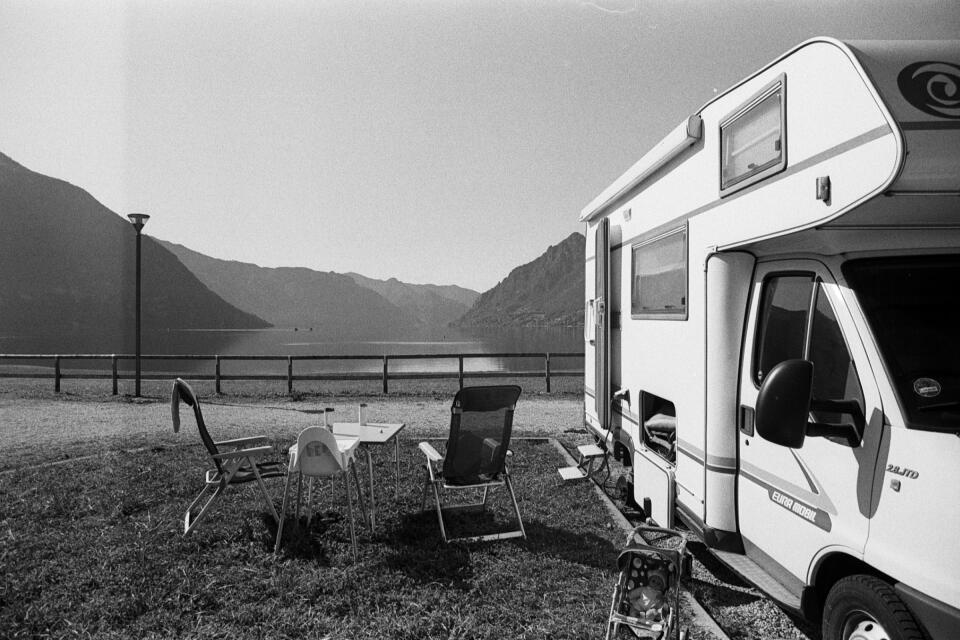 Our camper parked near a lake. We have our table and chairs next to it. It's sunny.