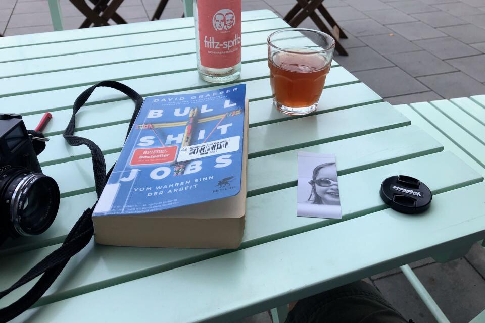 The book lying on a outdoor table at a cafe together with my camera and a glas of lemonade.