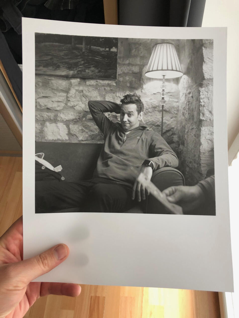 A man sitting on a sofa underneath a standing lamp, looking at the camera.