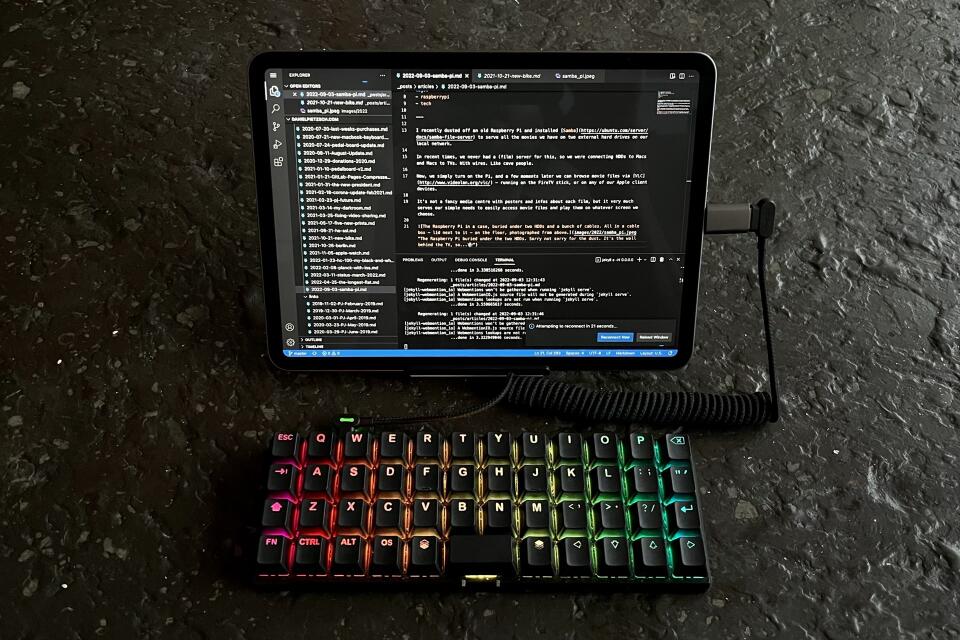 My Planck keyboard – rainbow-coloured backlit – connected to an iPad Pro showing the VS Code editor full screen. All on a black table photographed from above.